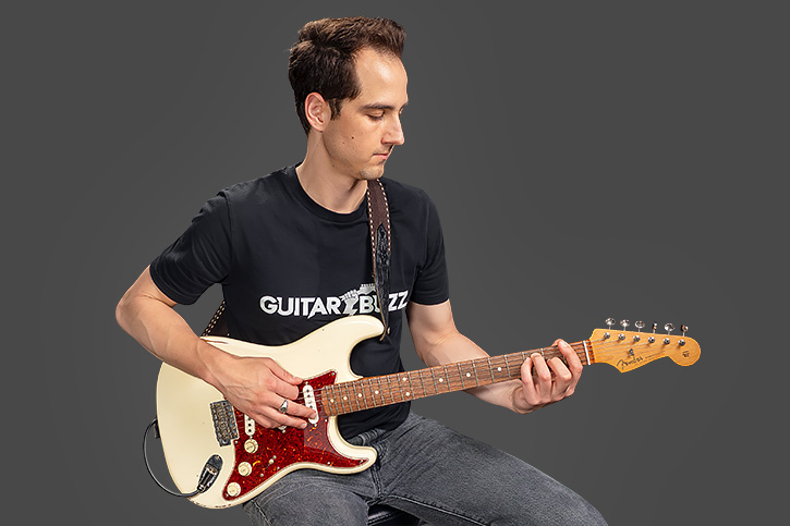 Alex sitting in playing position holding a guitar